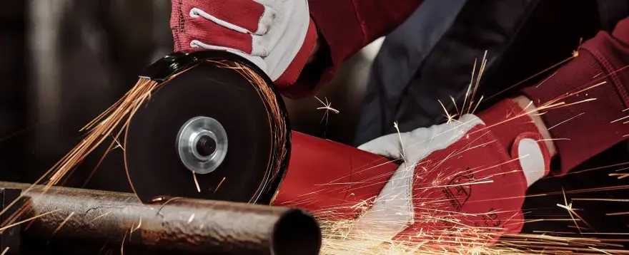 Ręce w czerwonych rękawicach używają szlifierki kątowej, by czym przeciąć metal. Iskry sypią się wokół.