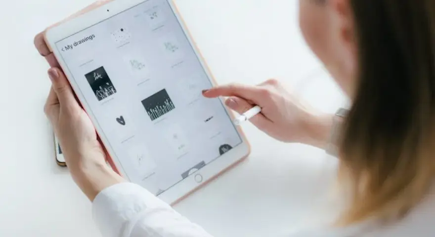 Kobieta tworzy rysowanie na iPadzie, przeglądając swoje prace. Stylus w dłoni sugeruje cyfrowe tworzenie.