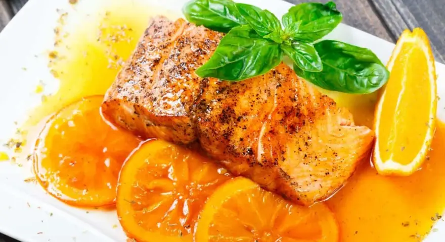 Delicioso salmón a la naranja, servido con rodajas de naranja fresca y hojas de albahaca.