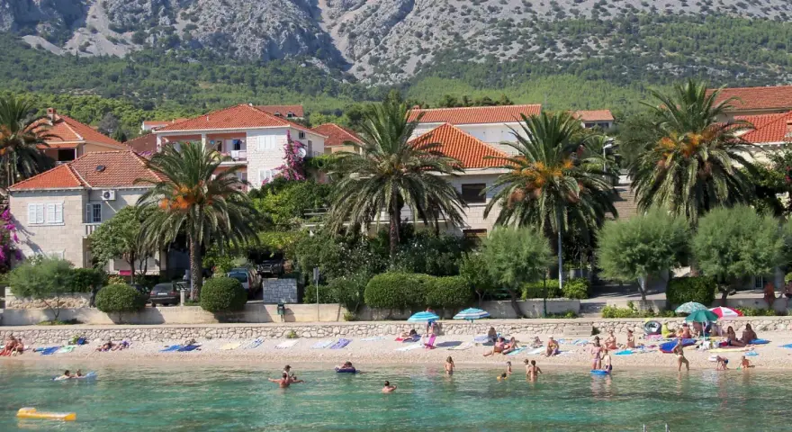 Plaża z palmami, domami i ludźmi kąpiącymi się w morzu.