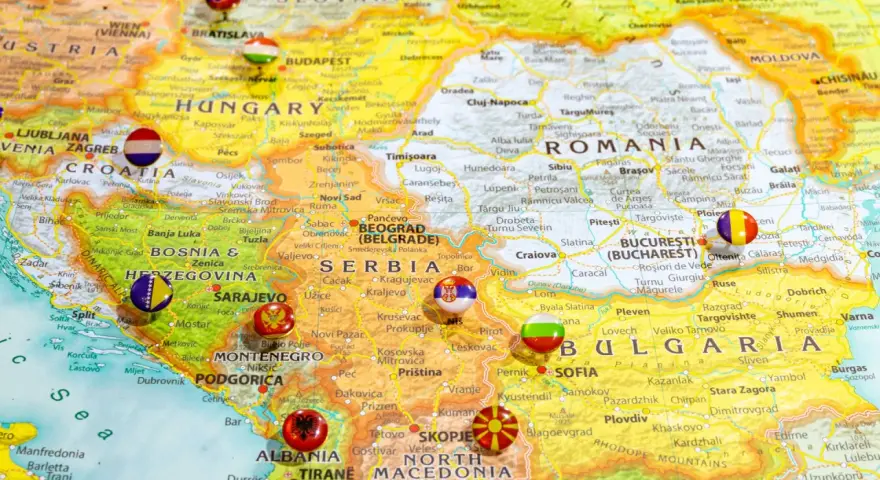 Mapa Europy z zaznaczonymi krajami bałkańskimi, w tym Serbią, Bułgarią i Rumunią, z flagami narodowymi w miejscach stolic.