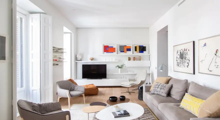 Salón moderno con sofás grises, mesas de centro y arte abstracto. Se aprecia la sutil diferencia entre blanco y blanco roto en paredes y carpintería.