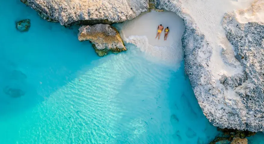 Para na plaży na wyspie Aruba, otoczonej turkusową wodą i skalistymi klifami. Idealne miejsce na relaks.
