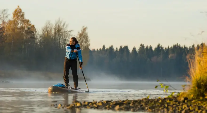 Mann auf Stand Up Paddle, achtet auf die ruhige Wasseroberfläche und die neblige Morgenstimmung.