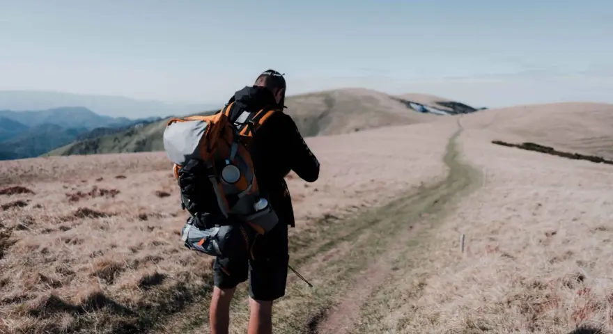 Uomo con zaino da trekking su un sentiero di montagna.