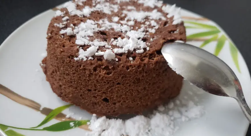 Un délicieux bowl cake au chocolat, saupoudré de sucre glace, prêt à être dégusté avec une cuillère.