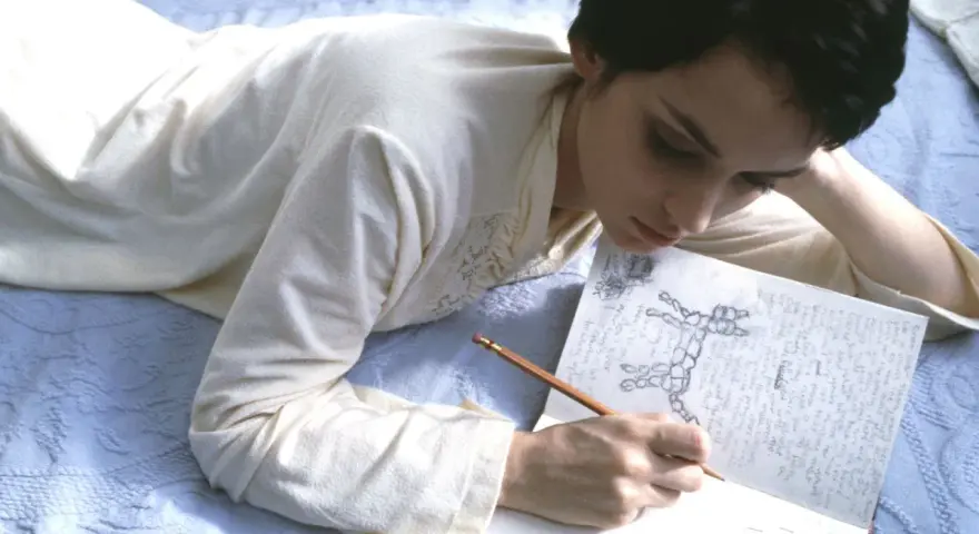 Junge Frau liegt auf dem Bett und schreibt mit Bleistift in ein Notizbuch. Sie ist vertieft in ihr diary entry schreiben.