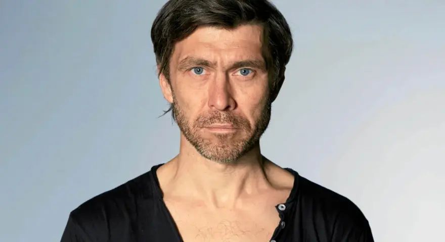 Marcin Czarnik, aktor o intensywnym spojrzeniu i niebieskich oczach, w czarnej koszulce.