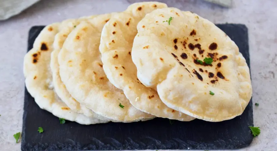 Frisch gebackenes pita brot, leicht gebräunt und mit Petersilie garniert, liegt auf einem dunklen Stein.