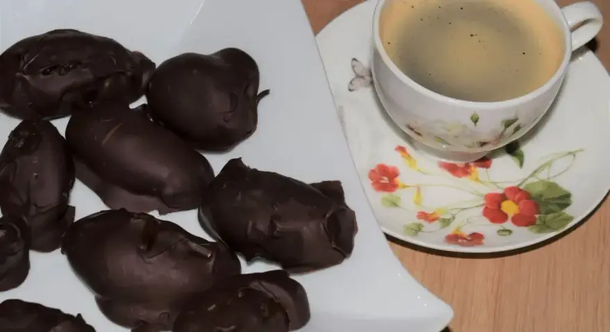 Czekoladowe śliwki z nalewki na talerzu, obok filiżanka kawy. Idealne, gdy zastanawiasz się, co zrobić ze śliwkami z nalewki.