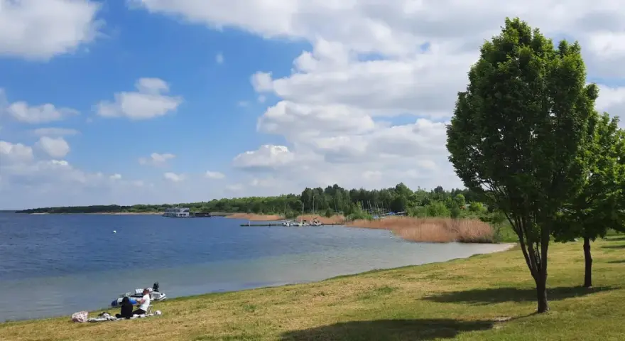 Sonniger Tag am Muldestausee. Menschen entspannen am Ufer, Boote liegen im Wasser. Perfekt zum Baden und Genießen.