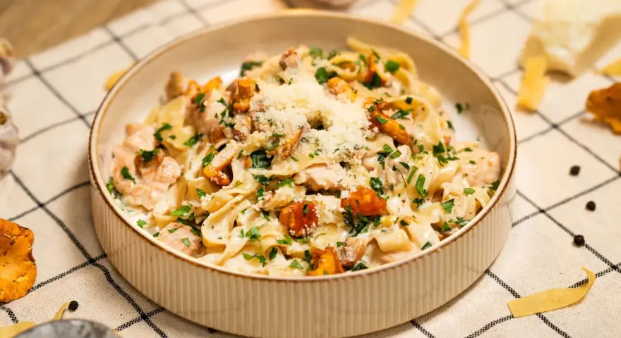 Pyszny makaron w sosie kurkowym z kawałkami kurczaka i posypany parmezanem.