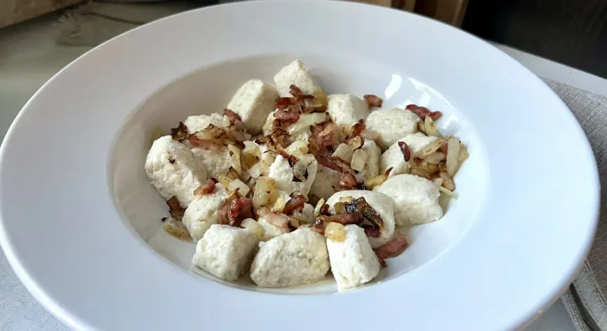 Pyszna keto kolacja z twarogiem w formie kluseczek, posypana chrupiącym boczkiem i cebulką.
