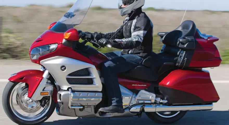 Mężczyzna w kasku jedzie lśniącym, czerwonym motocyklem turystycznym Honda Gold Wing.