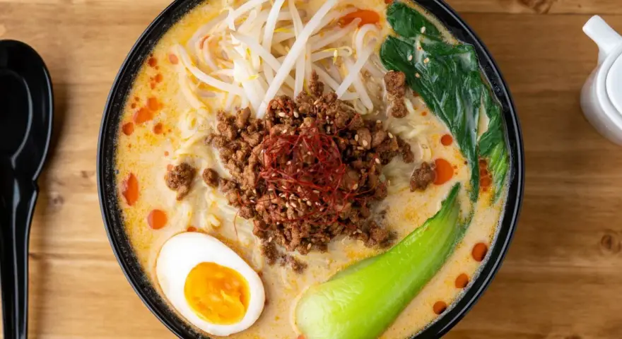 Miseczka ramenu tantanmen z mielonym mięsem, jajkiem, kiełkami i warzywami.
