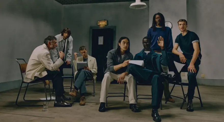 Grupo de hombres con un look business casual, sentados y de pie en una sala con un letrero de "EXIT".