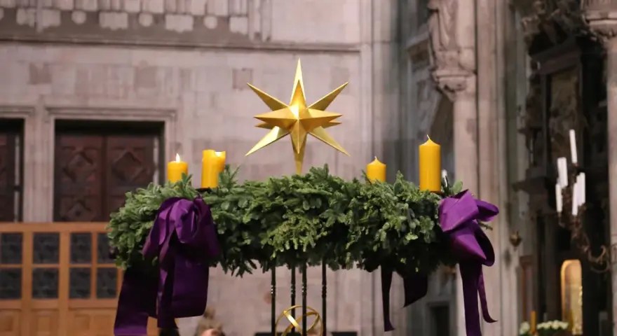 Ein Adventskranz mit vier gelben Kerzen und einem goldenen Stern, geschmückt mit lila Bändern. Seine Bedeutung liegt im Warten und Hoffen auf Weihnachten.