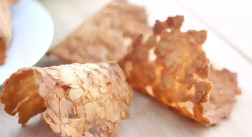 Trois tuiles aux amandes croustillantes, dorées et délicates, posées sur une planche en bois.
