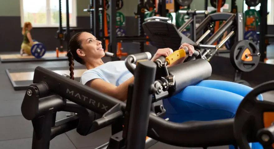 Femme souriante effectuant un hip thrust sur une machine de musculation, concentrée sur son entraînement.