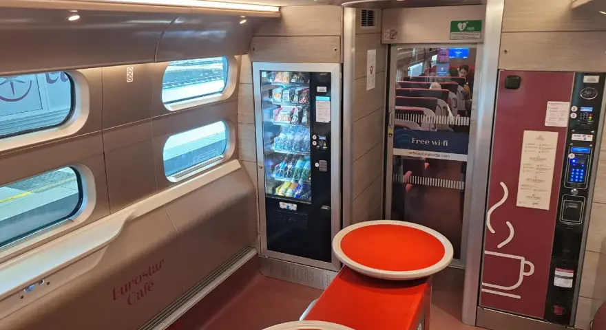 Interior of a Eurostar train from Amsterdam, featuring a cafe area with vending machines, seating, and windows looking out onto the tracks.