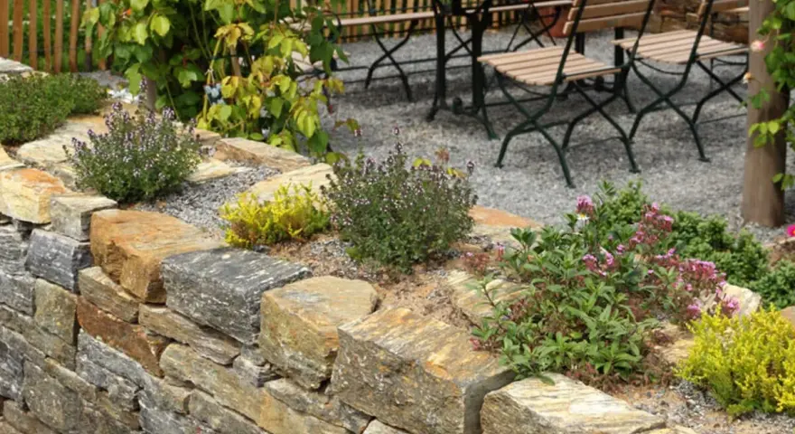 Natürliche Steinmauer mit Kräutern und Blumen, die schöne Ideen für den Garten bietet. Eine Sitzgruppe lädt zum Verweilen ein.