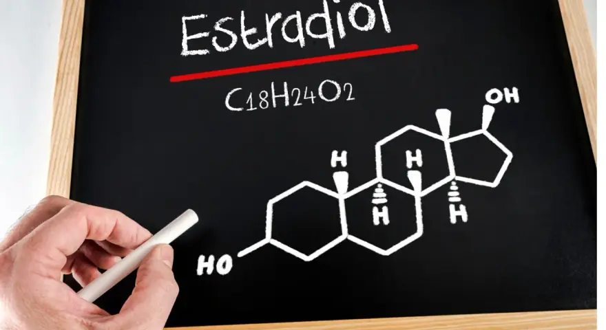 Estradiol co to za badanie? Na tablicy wzór chemiczny estradiolu (C18H24O2) i jego struktura. Ręka z kredą.