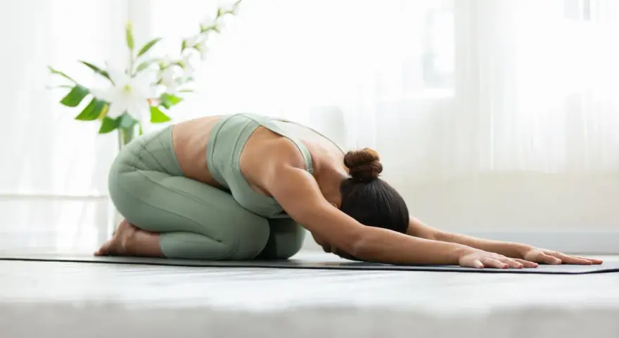 Donna in posizione di Balasana, una posa di yoga da seduti, rilassa la schiena e la mente.