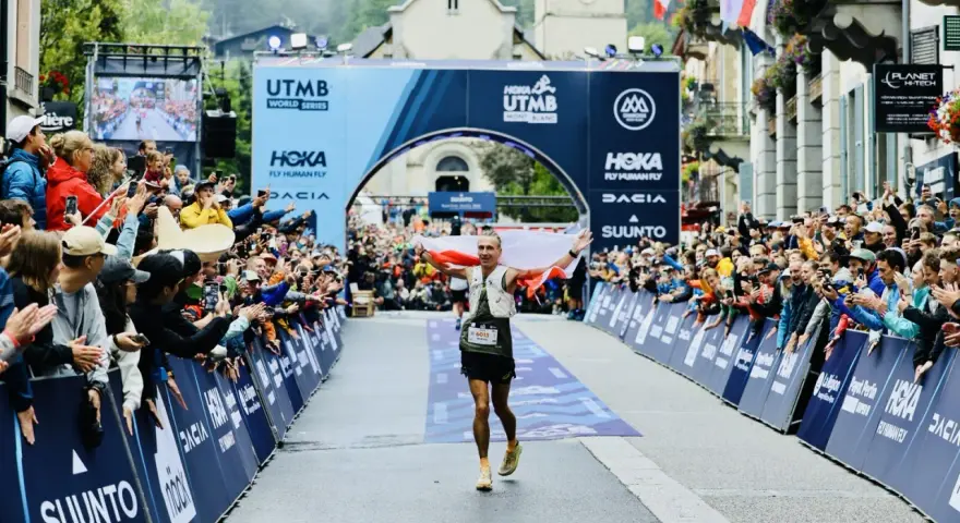 Biegacz z polską flagą przekracza metę UTMB Mont-Blanc. Tłum kibiców świętuje jego sukces.