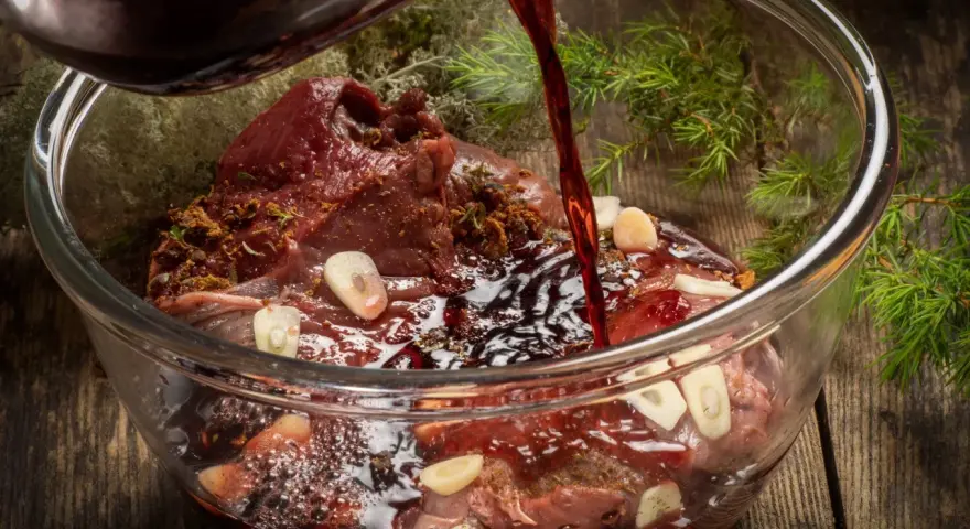 Ciemny płyn wlewa się do szklanej miski z karczkiem, czosnkiem i ziołami. Powstaje aromatyczna marynata do karczku.