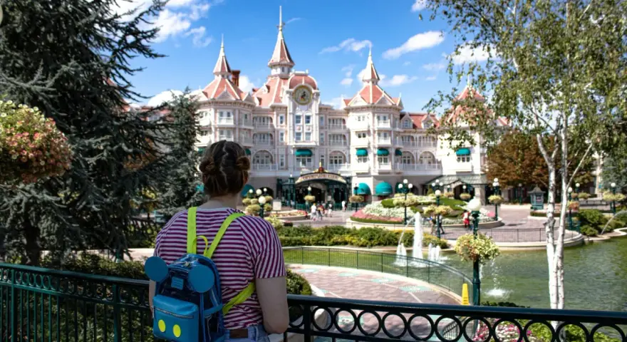 Dziewczyna z plecakiem w kształcie Myszki Miki patrzy na zamek w Disneyland Paris. Bilety do Disneyland Paris czekają na Ciebie!