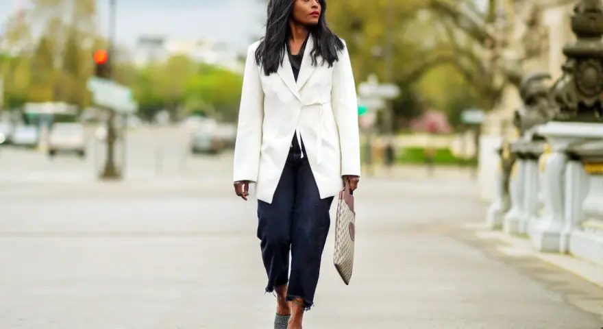 Mujer con estilo **smart casual** camina por la calle con un blazer blanco, jeans oscuros y sandalias de tacón.