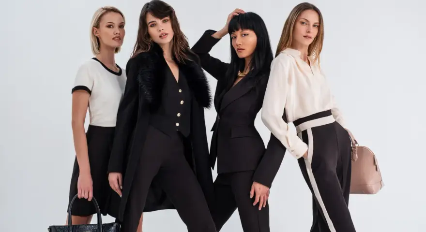 Quattro donne eleganti in abiti scuri e chiari, con borse di lusso, evocano lo spirito di Coco Chanel.