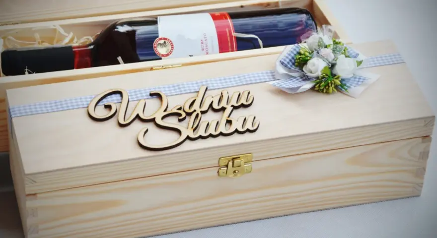 Drewniana skrzynka z butelką wina, ozdobiona wstążką i napisem "Wszystkiego najlepszego z okazji ślubu". Oryginalny prezent na ślub zamiast kwiatów.