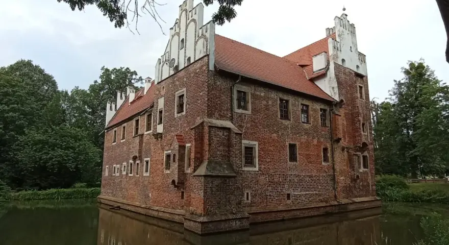 Zamek na wodzie w Wojnowicach, otoczony fosą, prezentuje ceglaną architekturę z białymi zdobieniami.