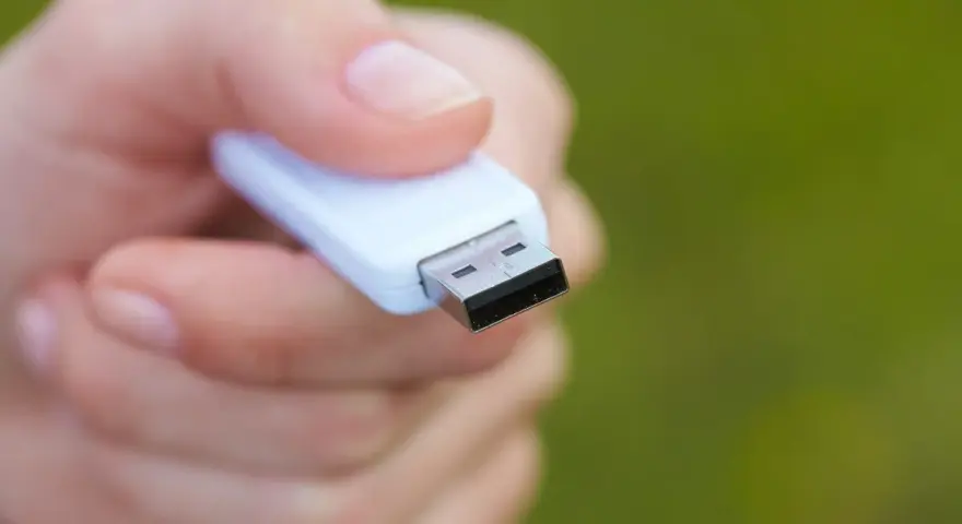 Dłoń trzyma biały pendrive, gotowy do formatowania NTFS.