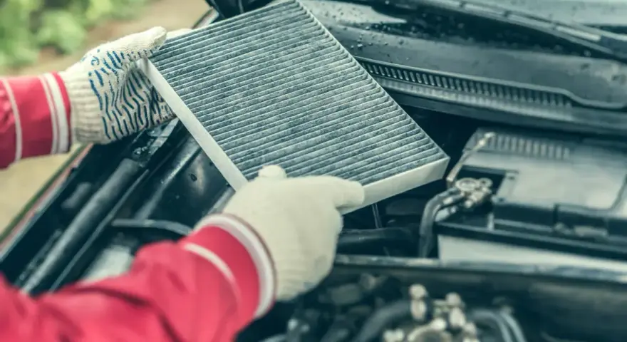 Hands in gloves hold a dirty cabin air filter, ready for replacement. This contrasts with the engine air filter, unseen but vital for car performance.
