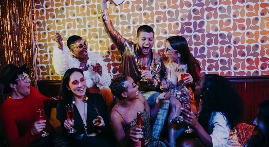 Grupa ludzi świętuje na imprezie w stylu lat 60. z drinkami i zabawnymi okularami.