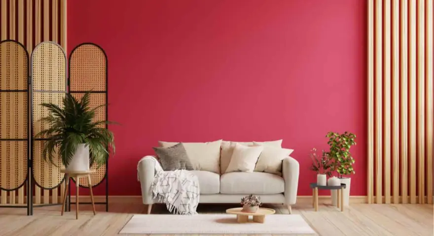 Un divano chiaro su un tappeto bianco, con una parete di un vivace viva magenta. Piante verdi e divisori in rattan completano l'arredamento.