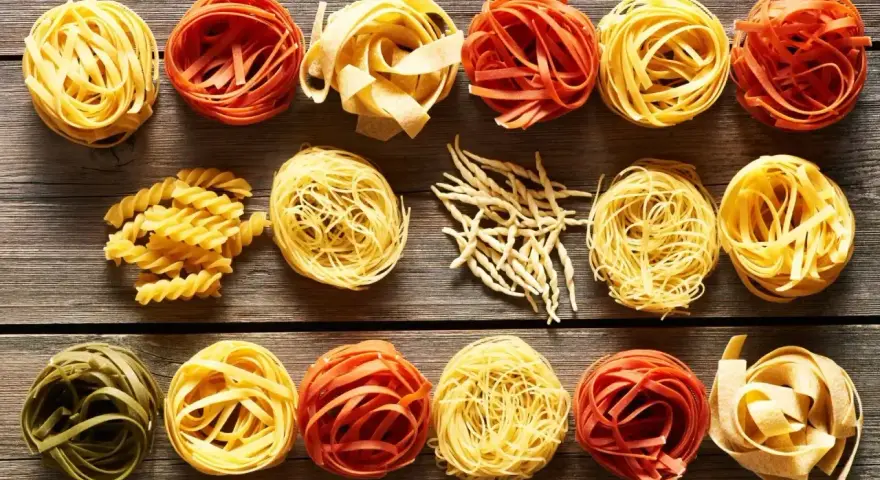 Różne rodzaje makaronu, w tym porcja makaronu spaghetti, ułożone na drewnianym blacie.