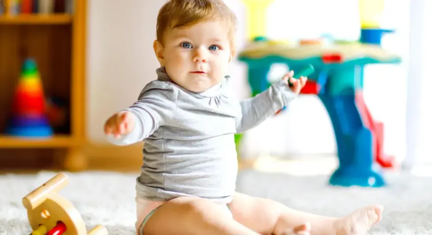 Ein neugieriges 8 Monate altes Baby mit blauen Augen sitzt auf einem flauschigen Teppich und spielt mit Spielzeug.