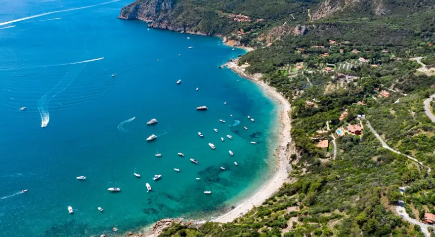 Baia con acque cristalline e numerose barche. Ville immerse nel verde e sentieri panoramici: ecco cosa vedere all'Argentario per una vacanza indimenticabile.