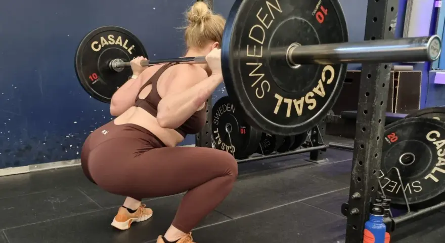 Kvinna utför en djup knäböj med skivstång. En del av hennes "russian squat routine" i gymmet.