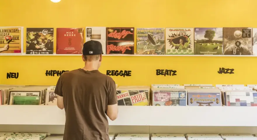 Mann durchstöbert Schallplatten in einem bunten Plattenladen in Berlin. Musikgenres wie HipHop, Reggae, Beatz und Jazz sind angeschrieben.