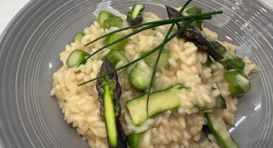 Kremowe risotto z zielonymi szparagami i szczypiorkiem na szarym talerzu.