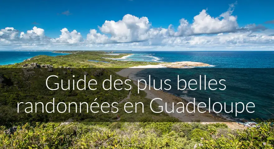 Paysage côtier luxuriant avec la mer bleue et des nuages blancs. Ce guide des plus belles randonnées en Guadeloupe vous invite à explorer ses montagnes verdoyantes.