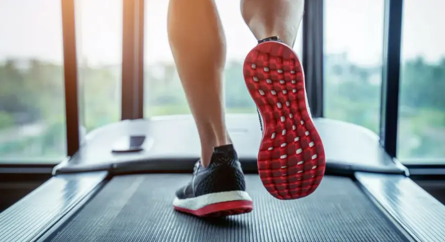 Gambe che corrono su un tapis roulant, con una scarpa rossa e nera in primo piano. Un'ottima immagine per chi vuole capire come iniziare a camminare.