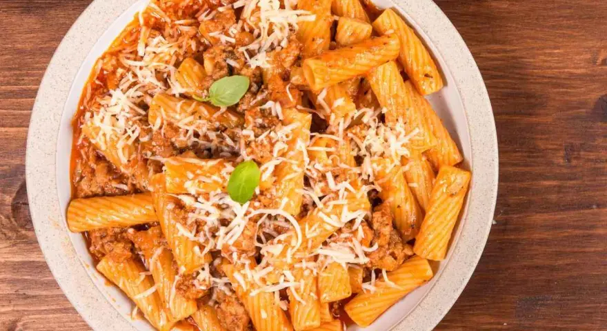 Un piatto invitante di pasta alla zozzona, con rigatoni conditi con un ricco ragù e abbondante parmigiano grattugiato, guarnito con basilico fresco.