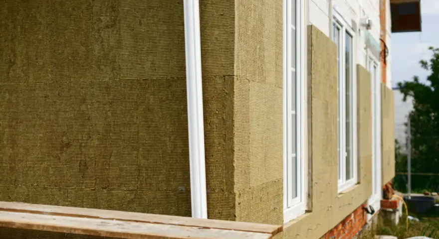 Detalle constructivo SATE: aislamiento de lana mineral en fachada, con ventanas blancas y tubería de desagüe.
