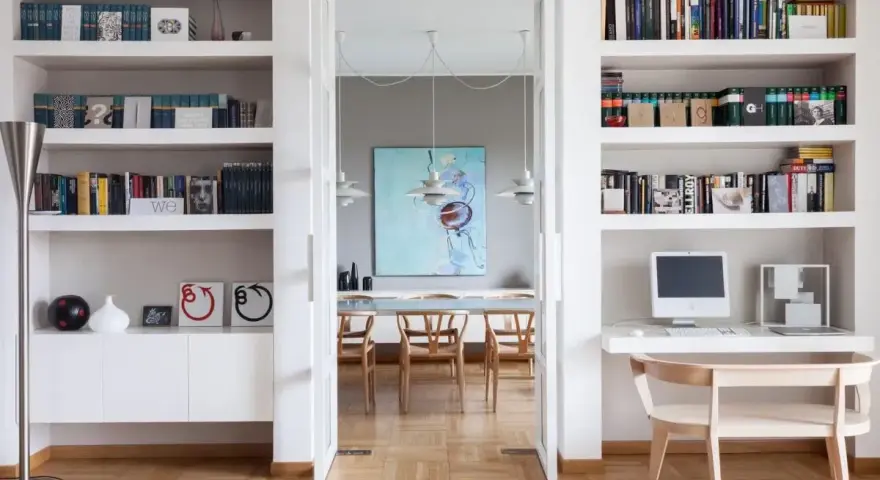 Ampia libreria in cartongesso con libri, computer e decorazioni. Si intravede una sala da pranzo con un quadro astratto.