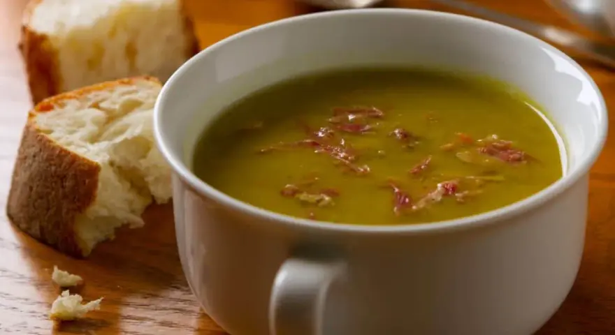 Un bol de soupe de pois cassés fumante, garnie de lardons, avec du pain croustillant à côté. Un délice réconfortant.
